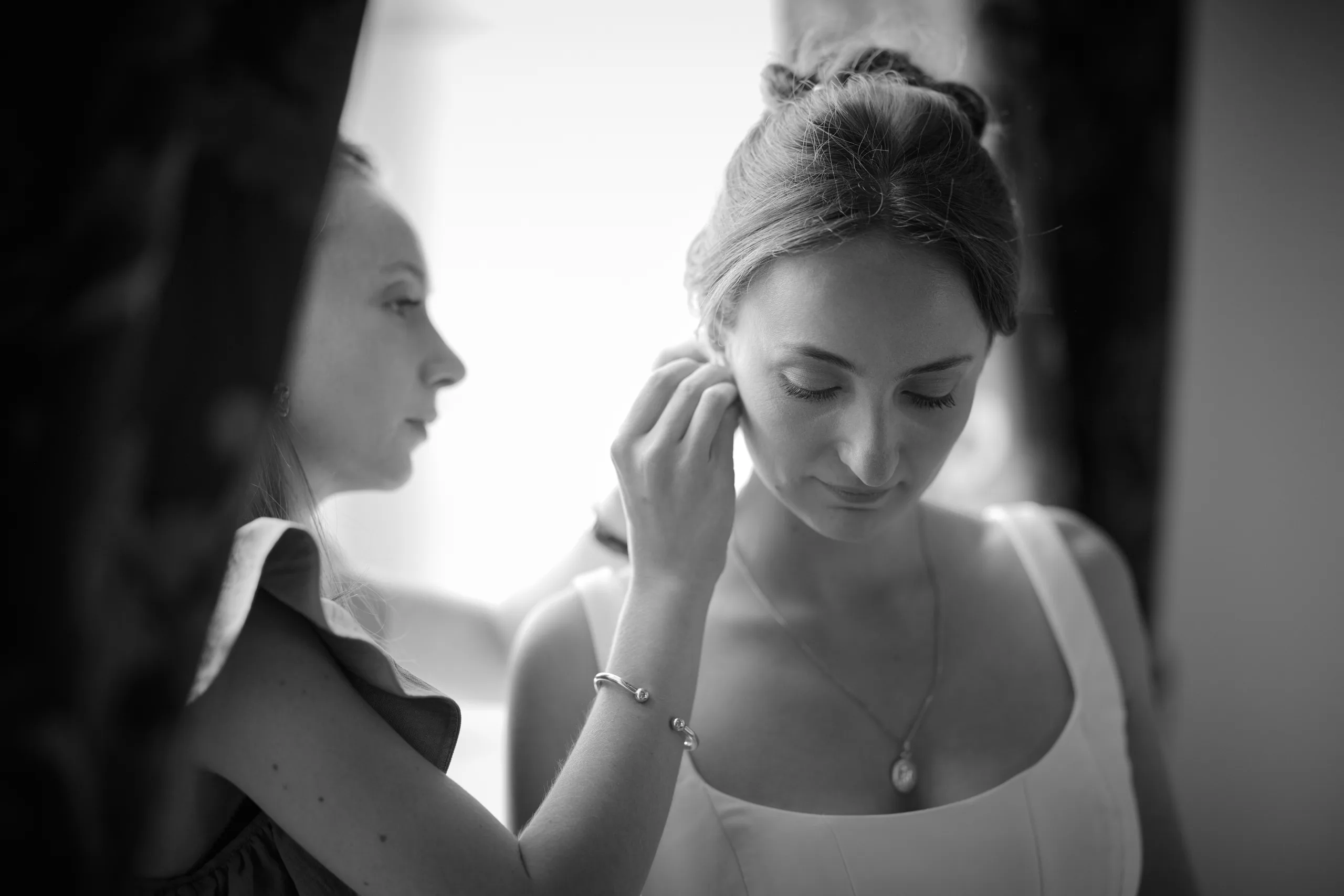 Une femme maquille les yeux d’une autre, en noir et blanc