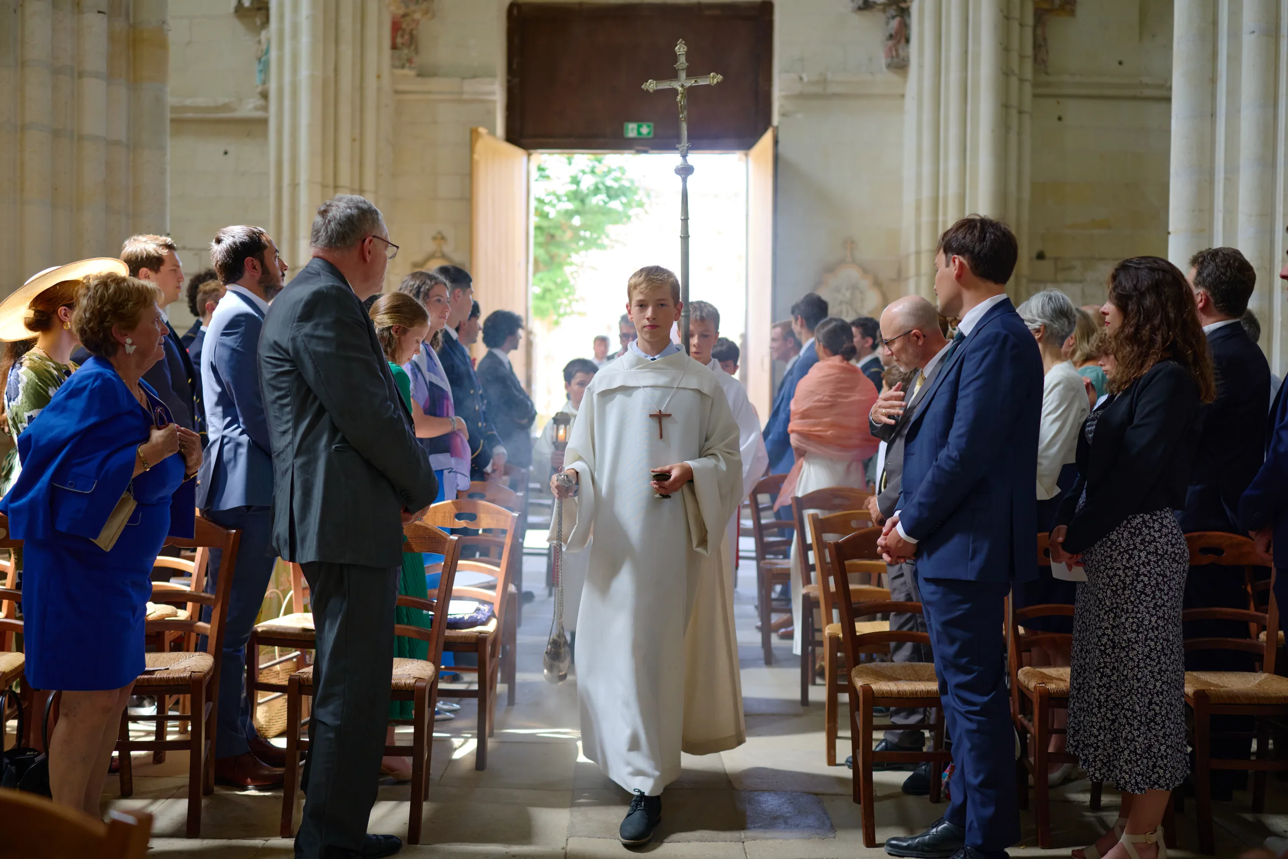 Un prêtre avance dans l’allée tandis que les invités se tiennent debout
