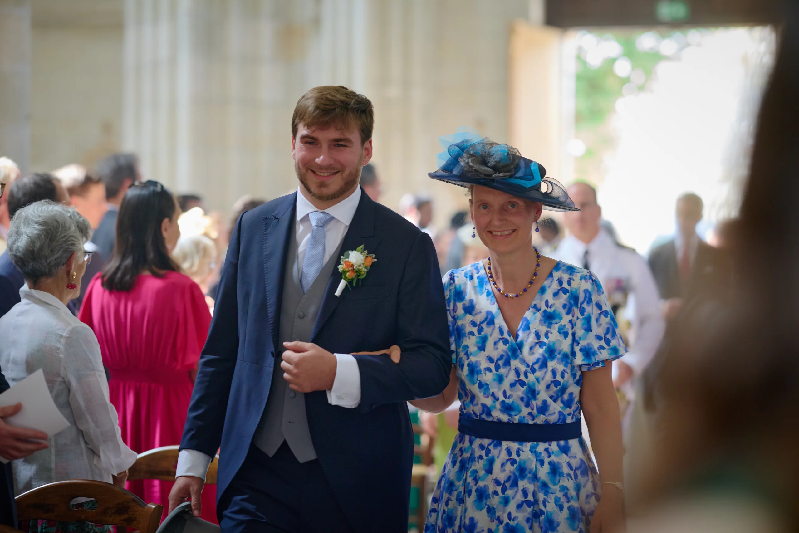 Le marié marche dans l’église avec une invitée en chapeau bleu