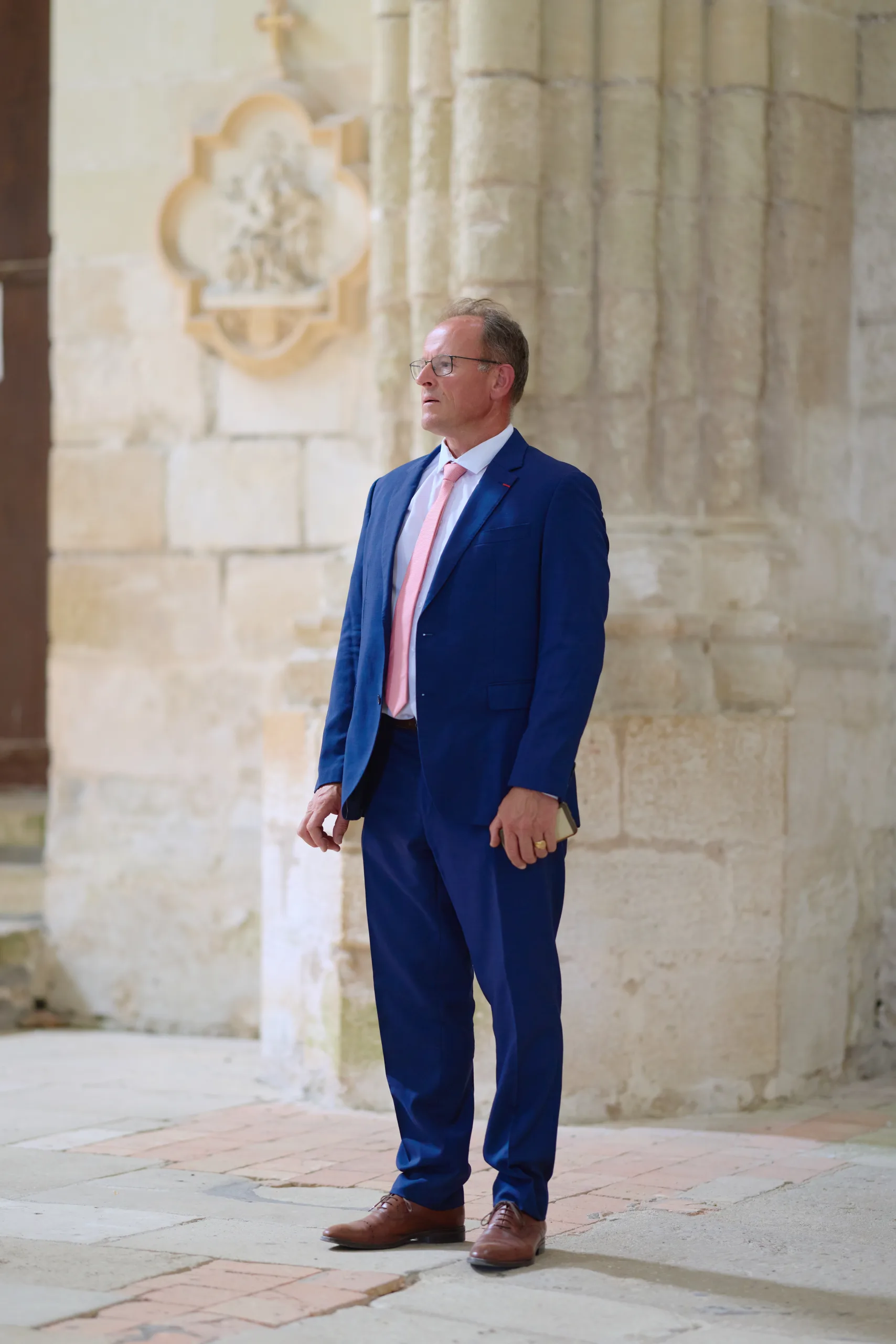 Homme en costume bleu debout près du mur de l’église