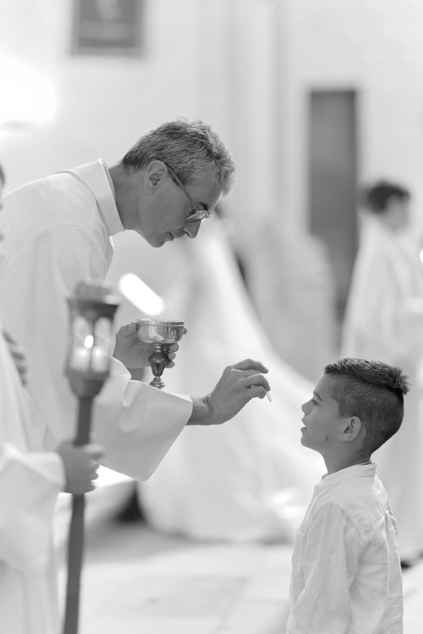 Prêtre donnant la communion à un enfant, en noir et blanc