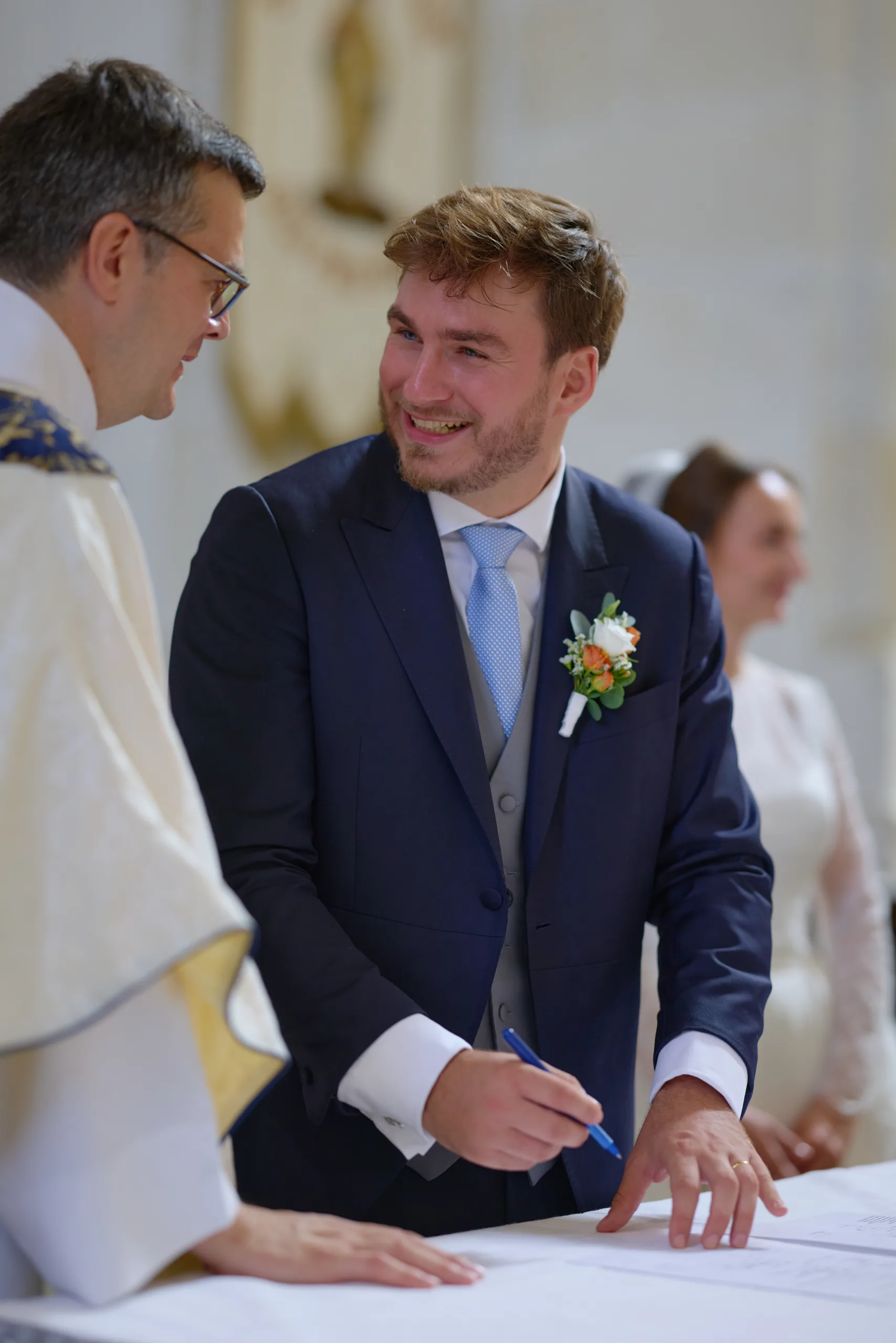 Homme en costume souriant devant un prêtre