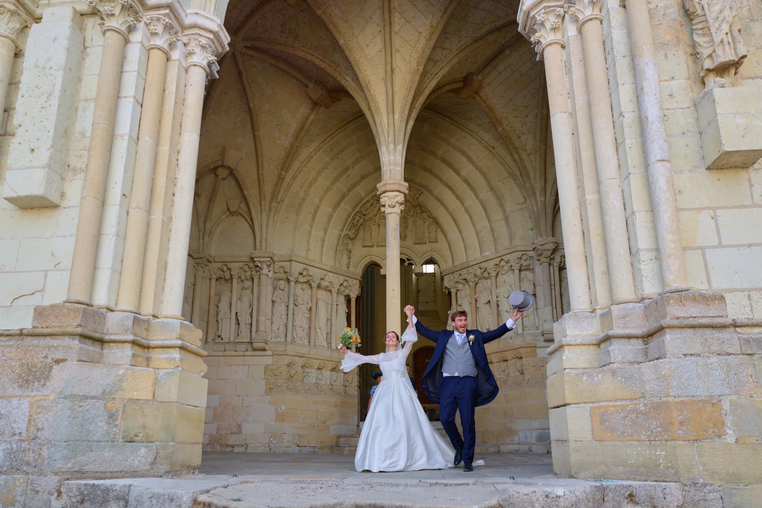 Les mariés lèvent les bras sous le porche de l’église