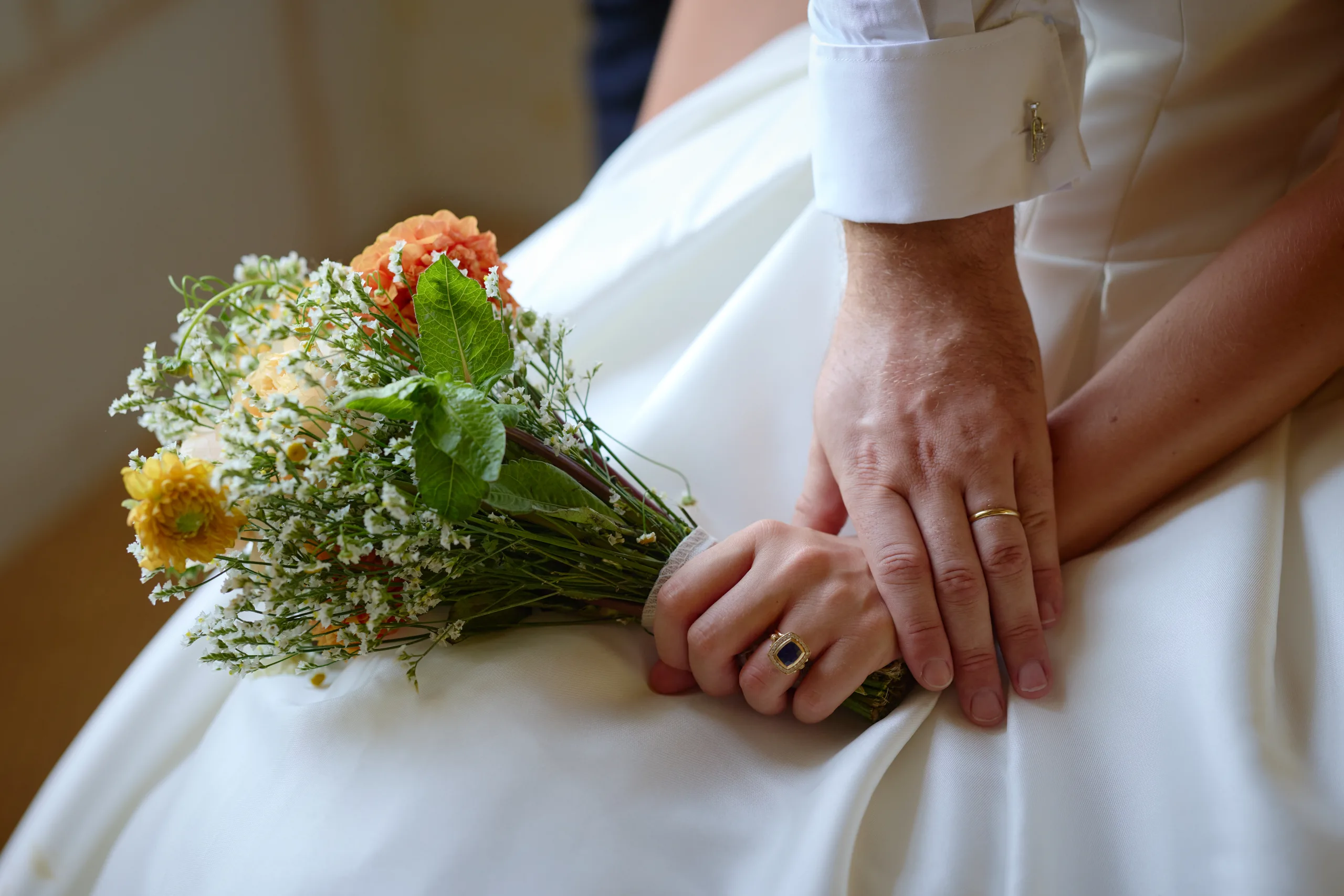 Le bouquet et les mains des mariés sur la robe de la mariée