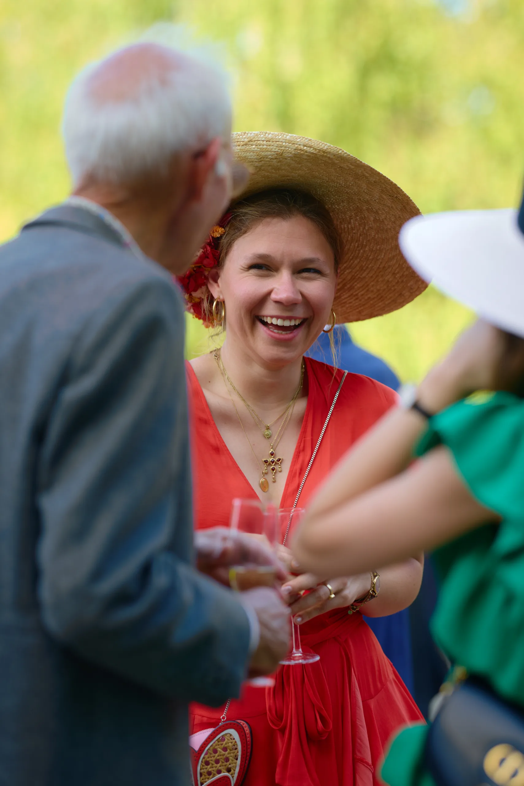 Une invitée en robe rouge et chapeau de paille sourit