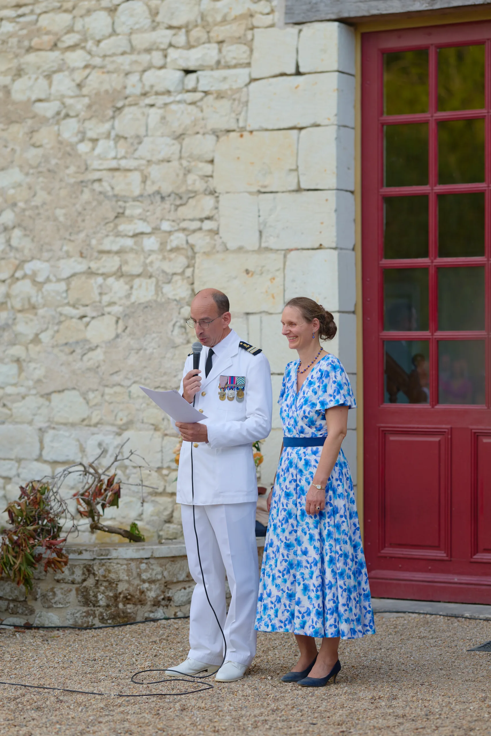 Un homme en uniforme blanc et une femme devant une porte rouge