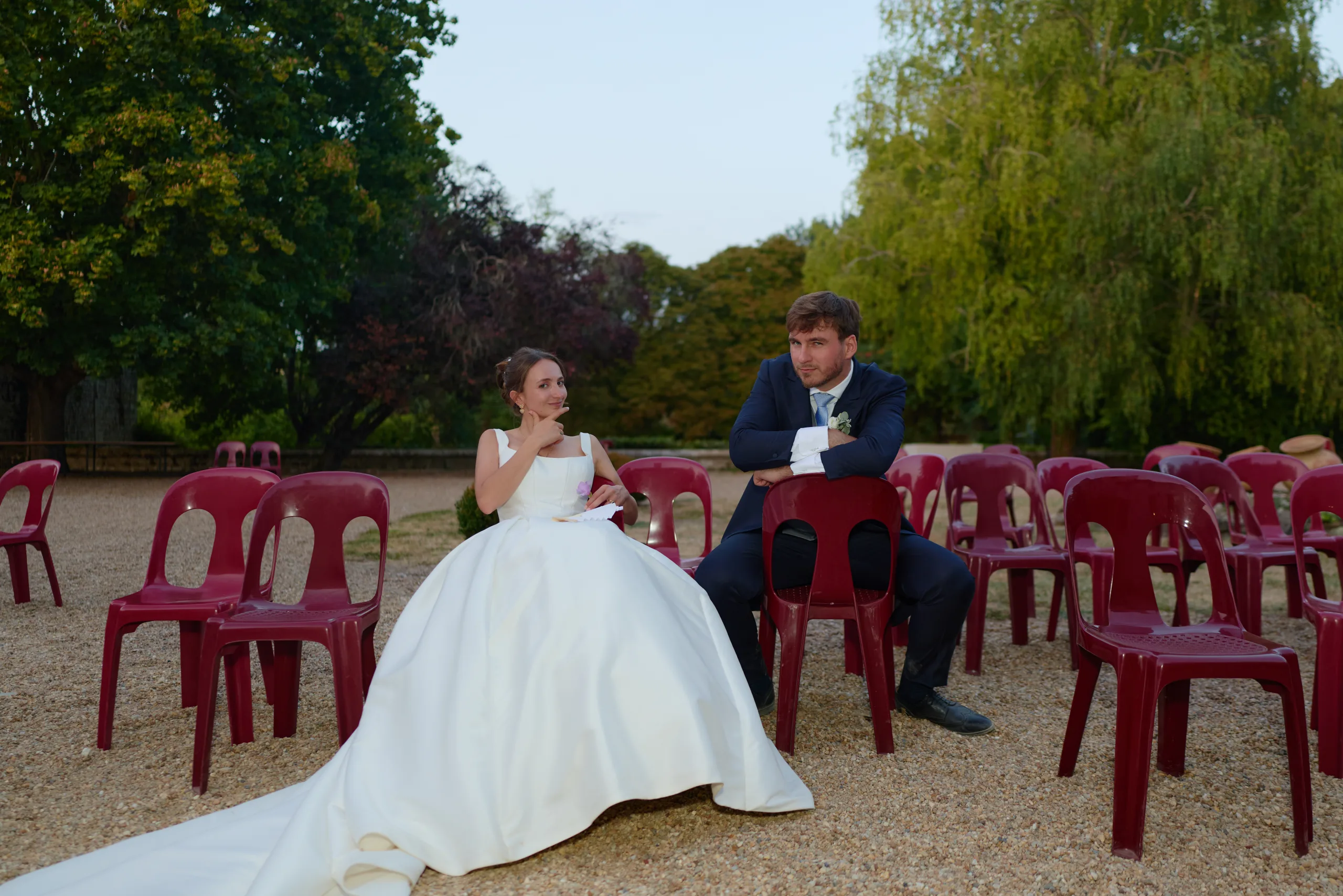 Les mariés assis parmi des chaises rouges dans la cour