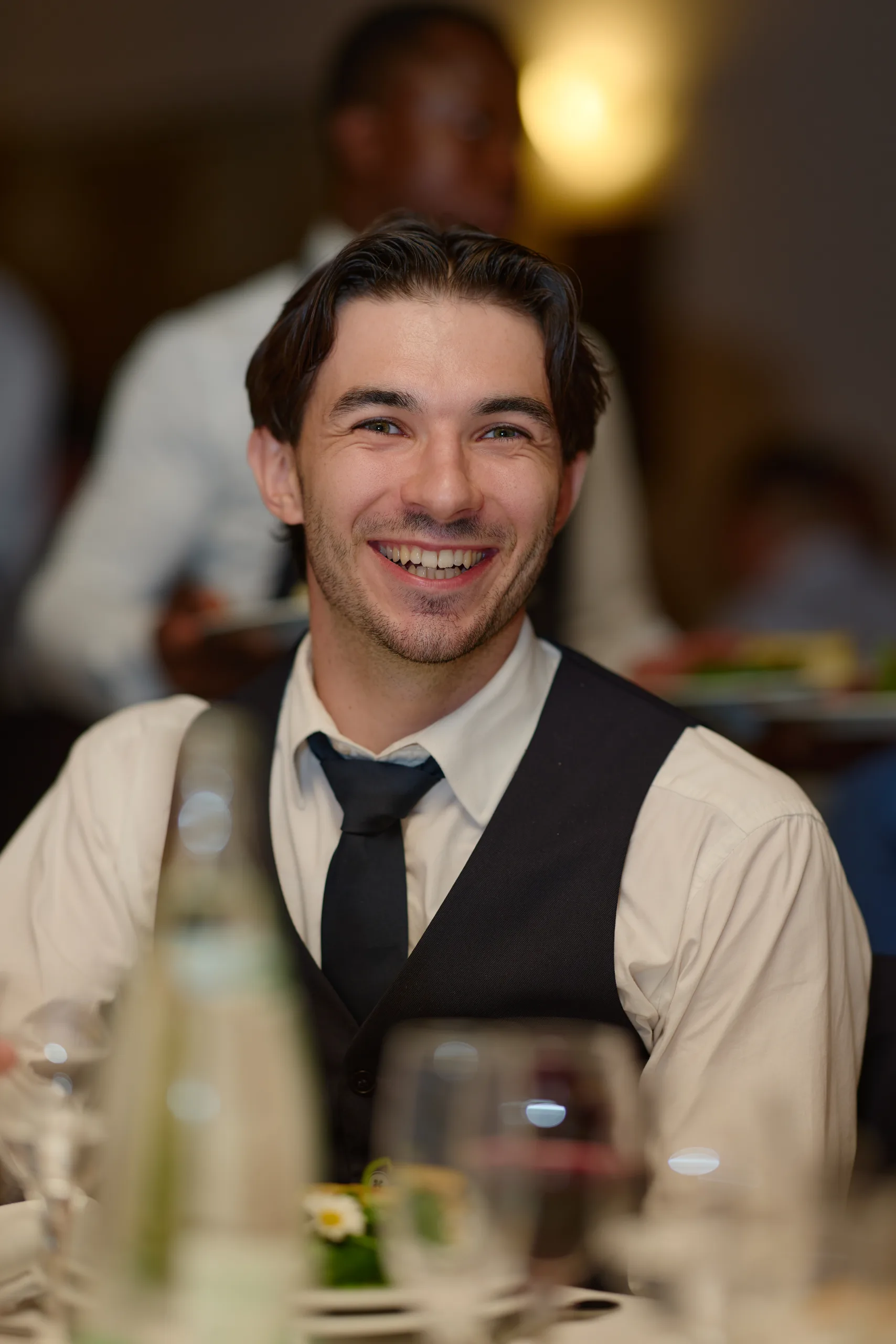 Un invité en gilet et cravate sourit pendant le repas