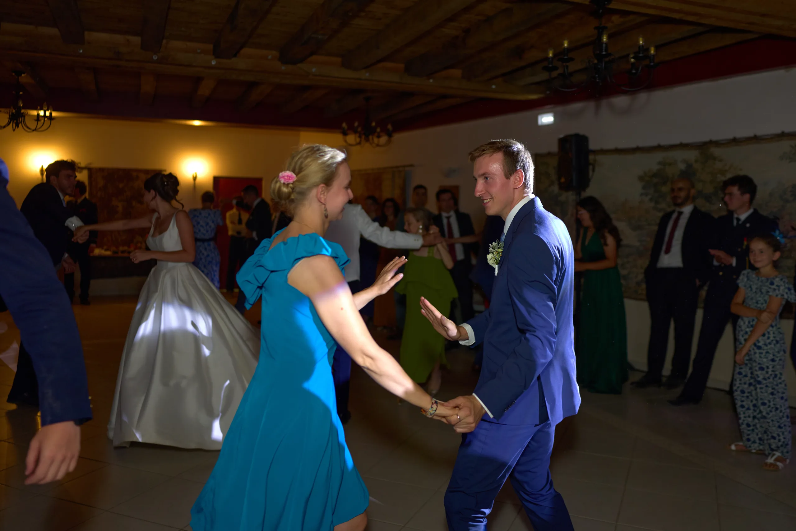 Le marié et une invitée en robe bleue se tiennent les mains en dansant
